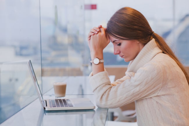 Deprimerad ung kvinna framför laptop med knutna händer i pannan.