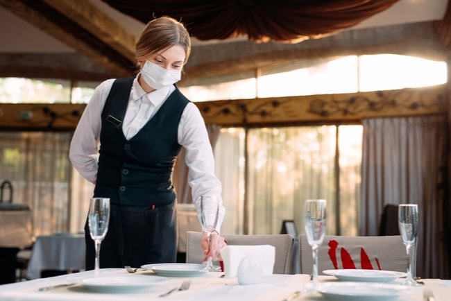 servitris med munskydd dukar bort på restaurang