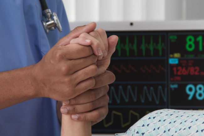 En sjuksköterskas hand håller en sängliggande patients hand
