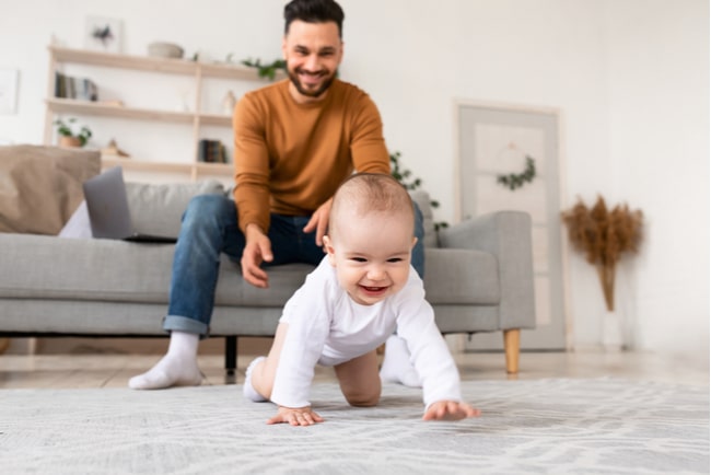 En pappa leker med sitt barn som kryper på golvet.